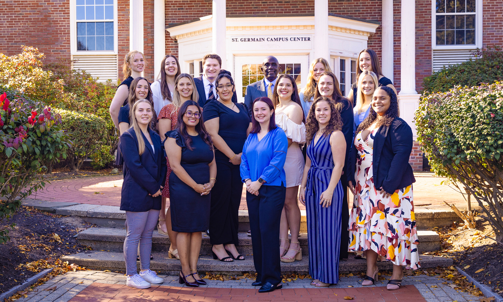 Sixteen honorees dressed formally stand with President Johnson in front of the St. Germain Campus Center